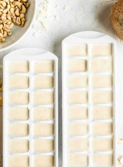 2 white ice cube trays filled with frozen coconut cubes on a white counter top.