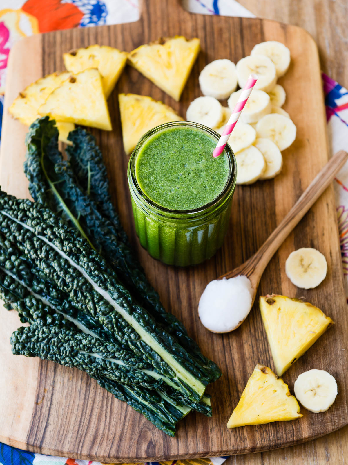 Green smoothie in a glass jar with surrounding ingredients: bananas, pineapple, and fresh greens.