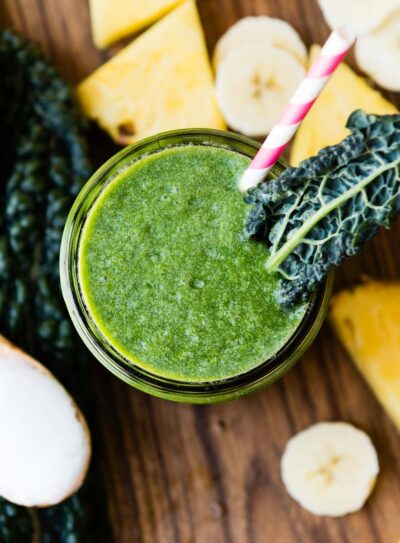 Top-down view of a coconut oil smoothie garnished with a kale leaf, surrounded by fresh ingredients.