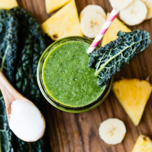 Top-down view of a coconut oil smoothie garnished with a kale leaf, surrounded by fresh ingredients.