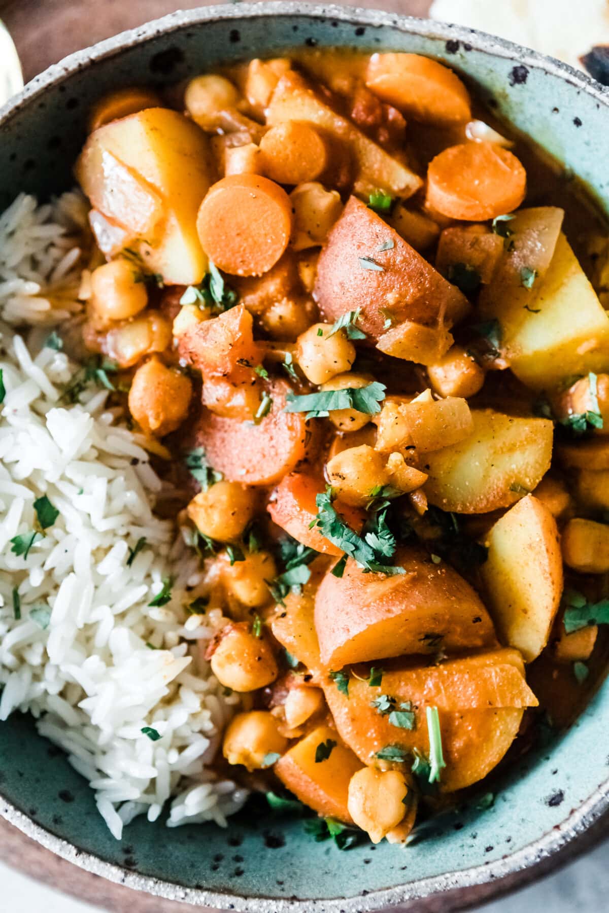 seasoned potatoes and chickpeas in a bowl with rice and topped with cilantro.