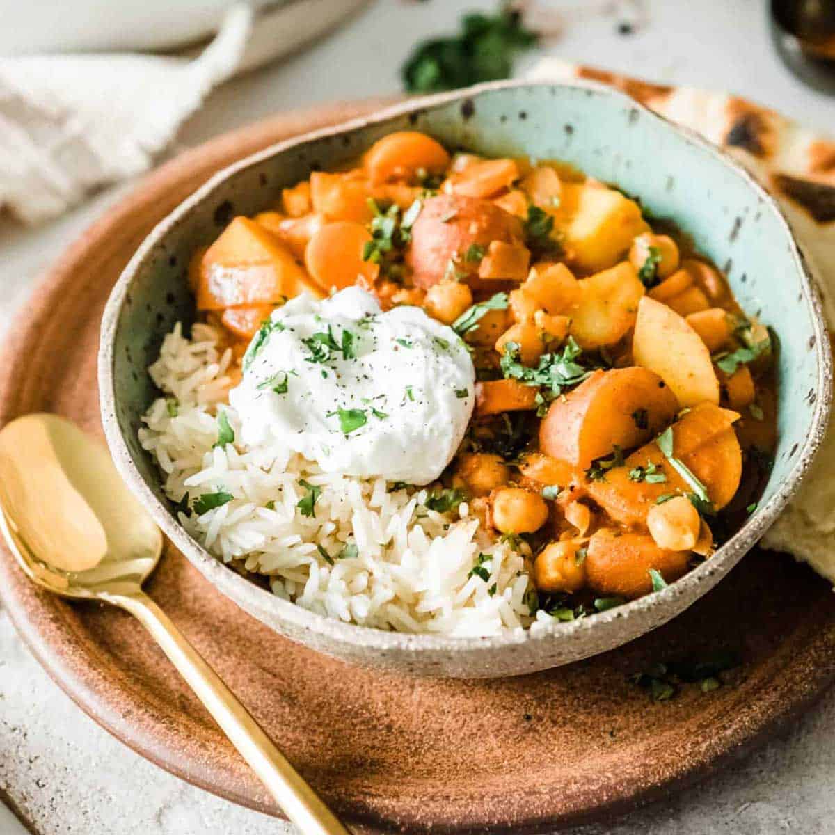 vegan potato curry with cashew cream and rice in a bowl with a gold spoon.
