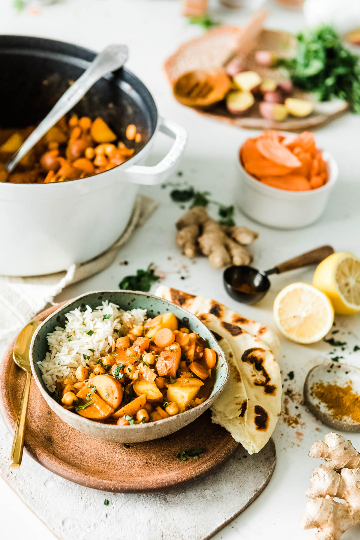 Bowl of creamy potato curry and rice, alongside naan bread, with recipe ingredients in the background.