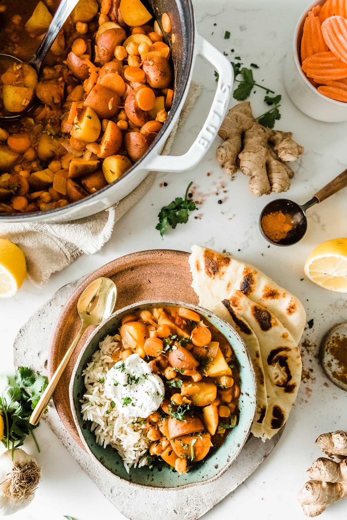 Creamy potato curry in a bowl, ready to eat, next to a pot full of the same.
