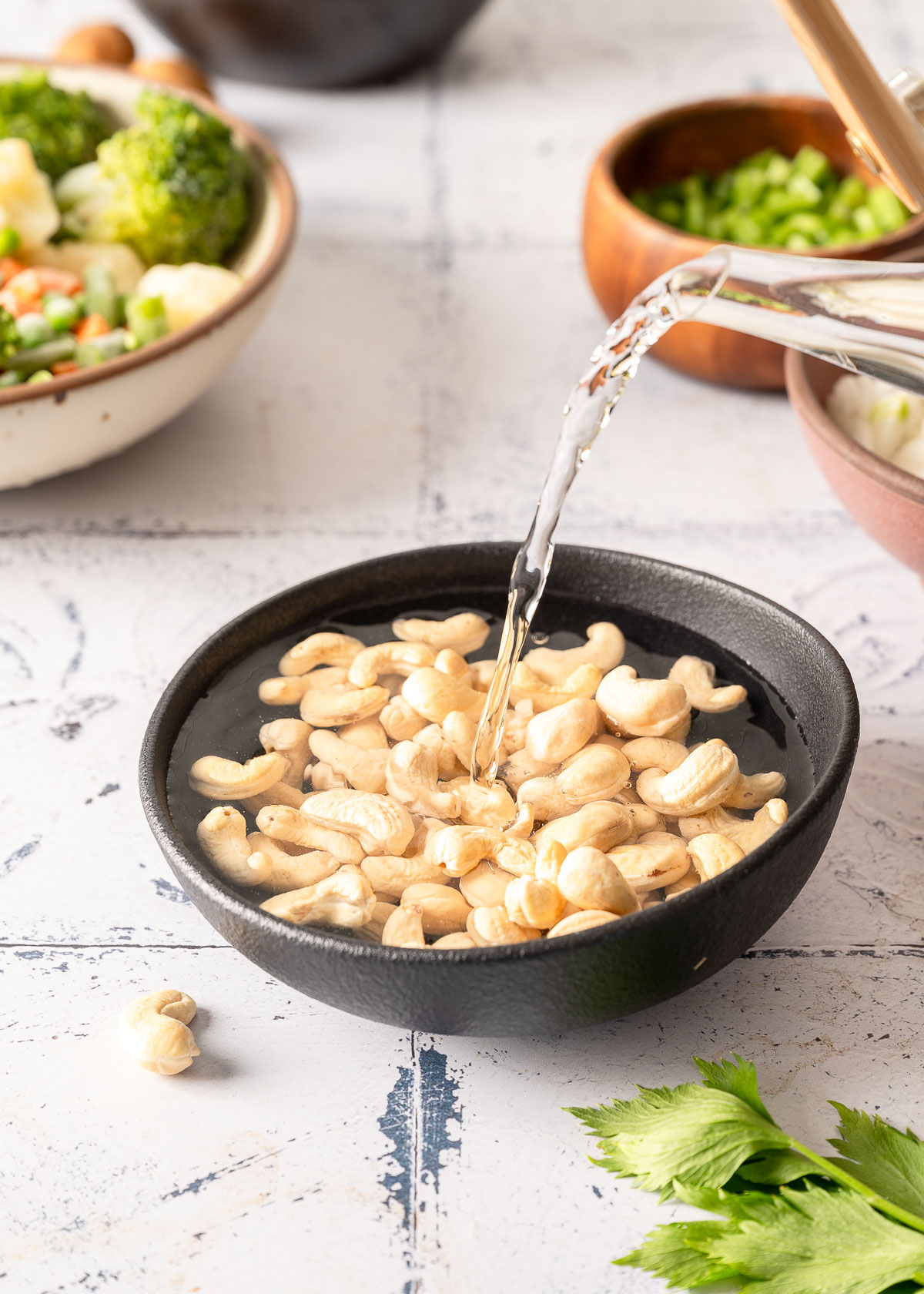 Hot water being poured into a black bowl filled with cashews.
