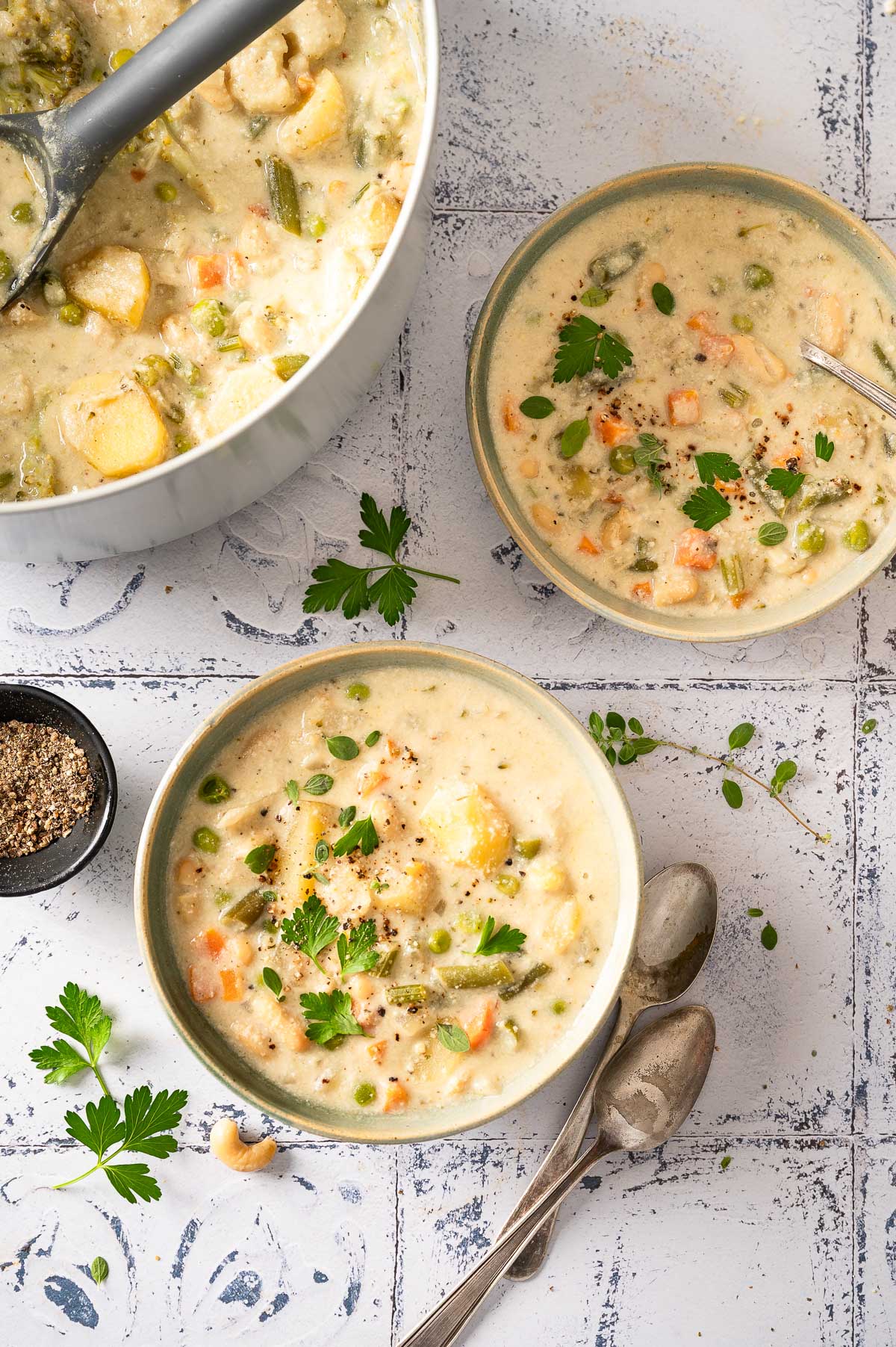 A pot and two bowls filled with creamy vegetable soup, garnished with fresh parsley.