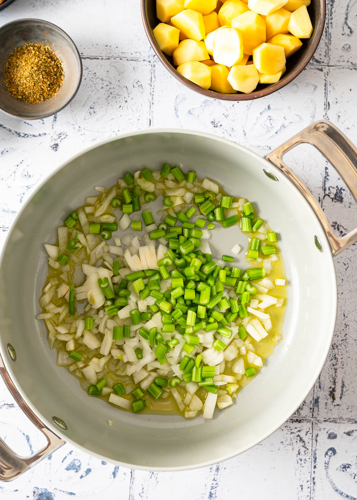 A gray pan with onions and celery being sautéed in avocado oil.
