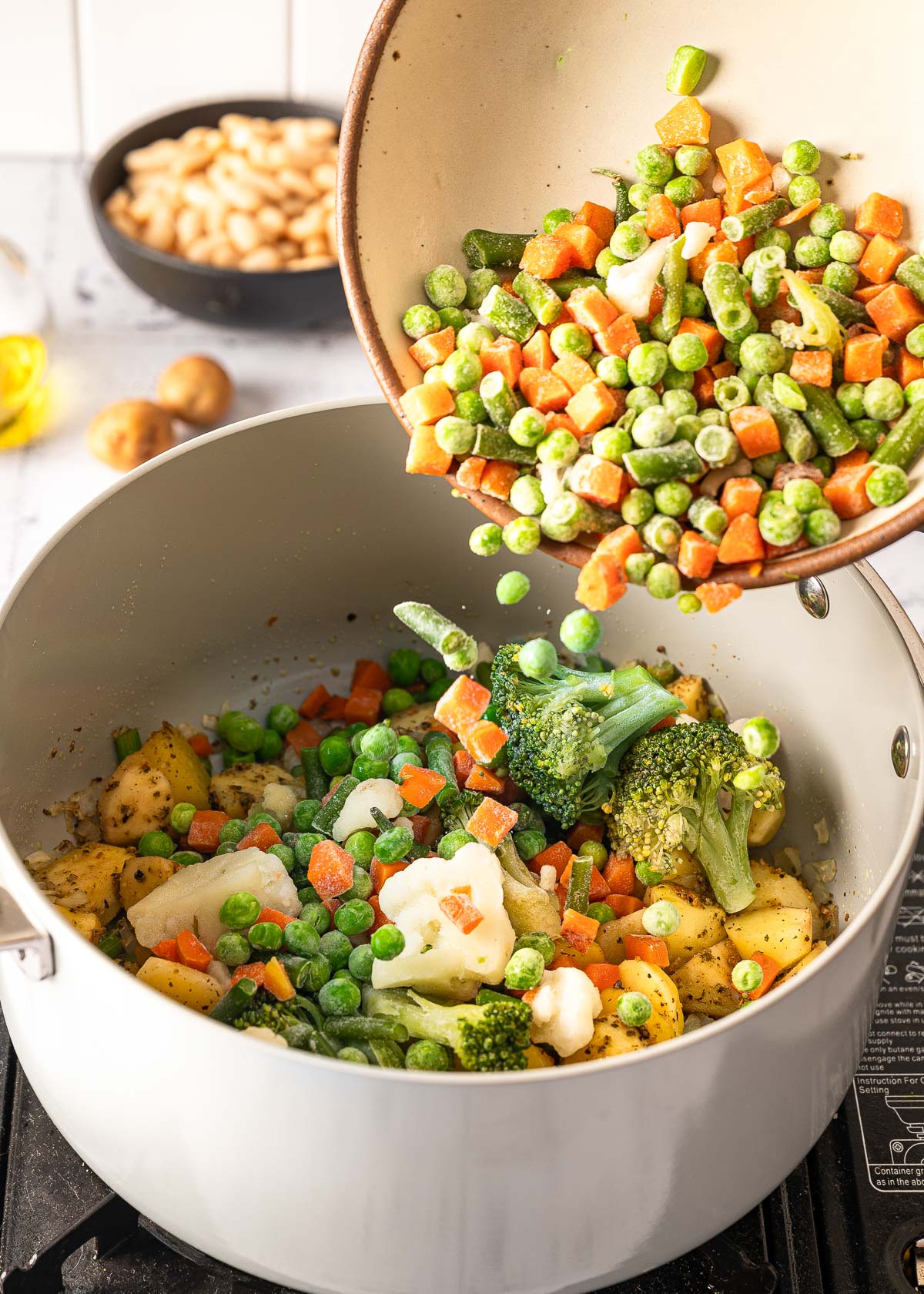 A bowl of frozen vegetables being poured into a gray pan.