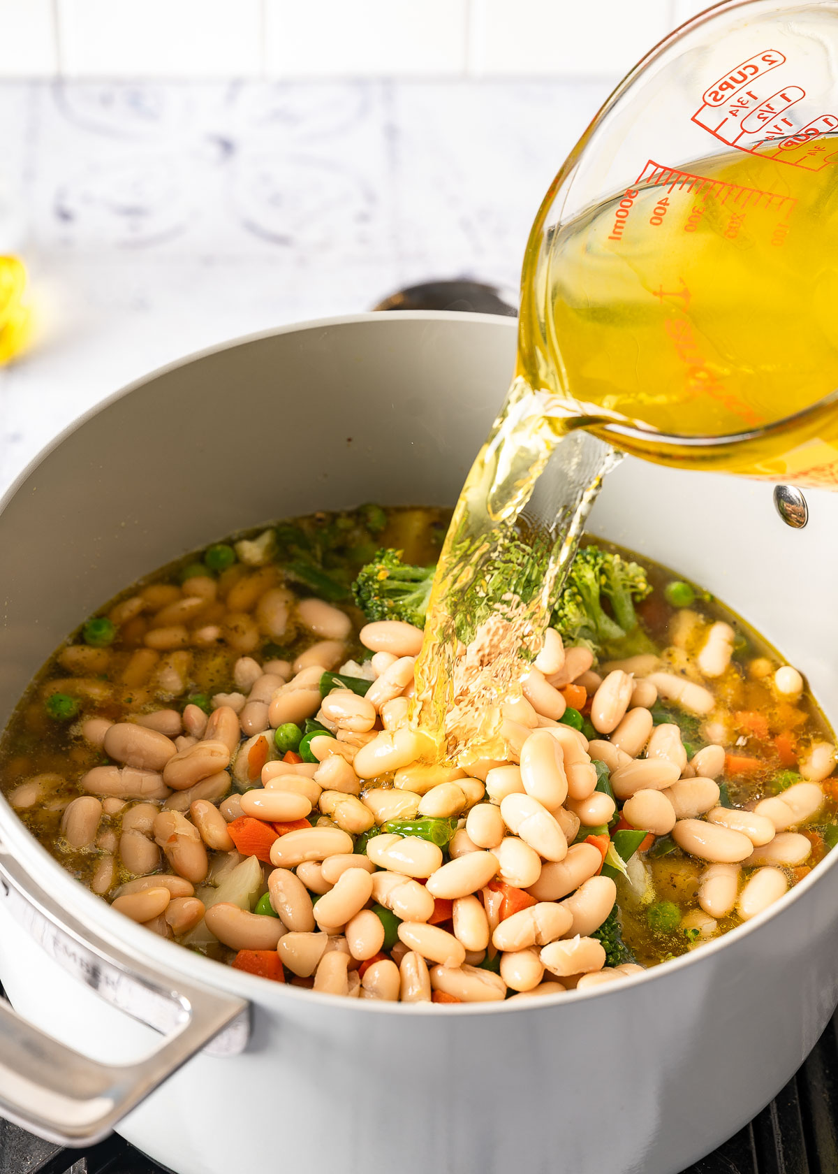 Vegetable broth being poured into a creamy vegetable soup while it is cooking.