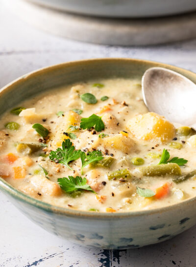 A bowl of ready-to-eat creamy vegetable soup with a silver spoon.