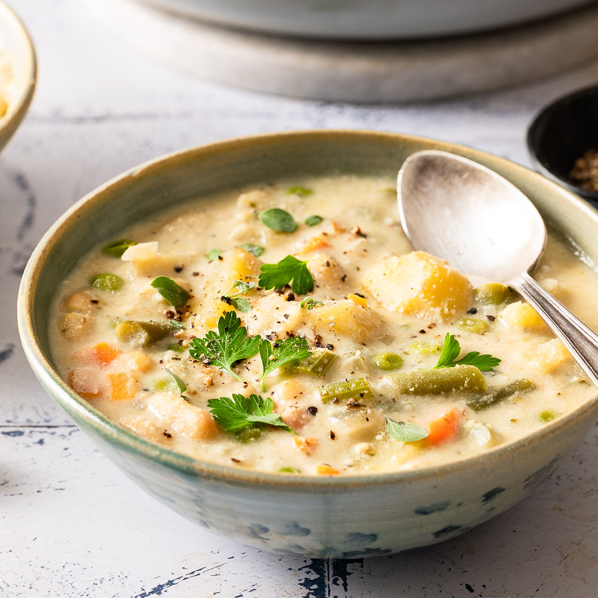 A bowl of ready-to-eat creamy vegetable soup with a silver spoon.