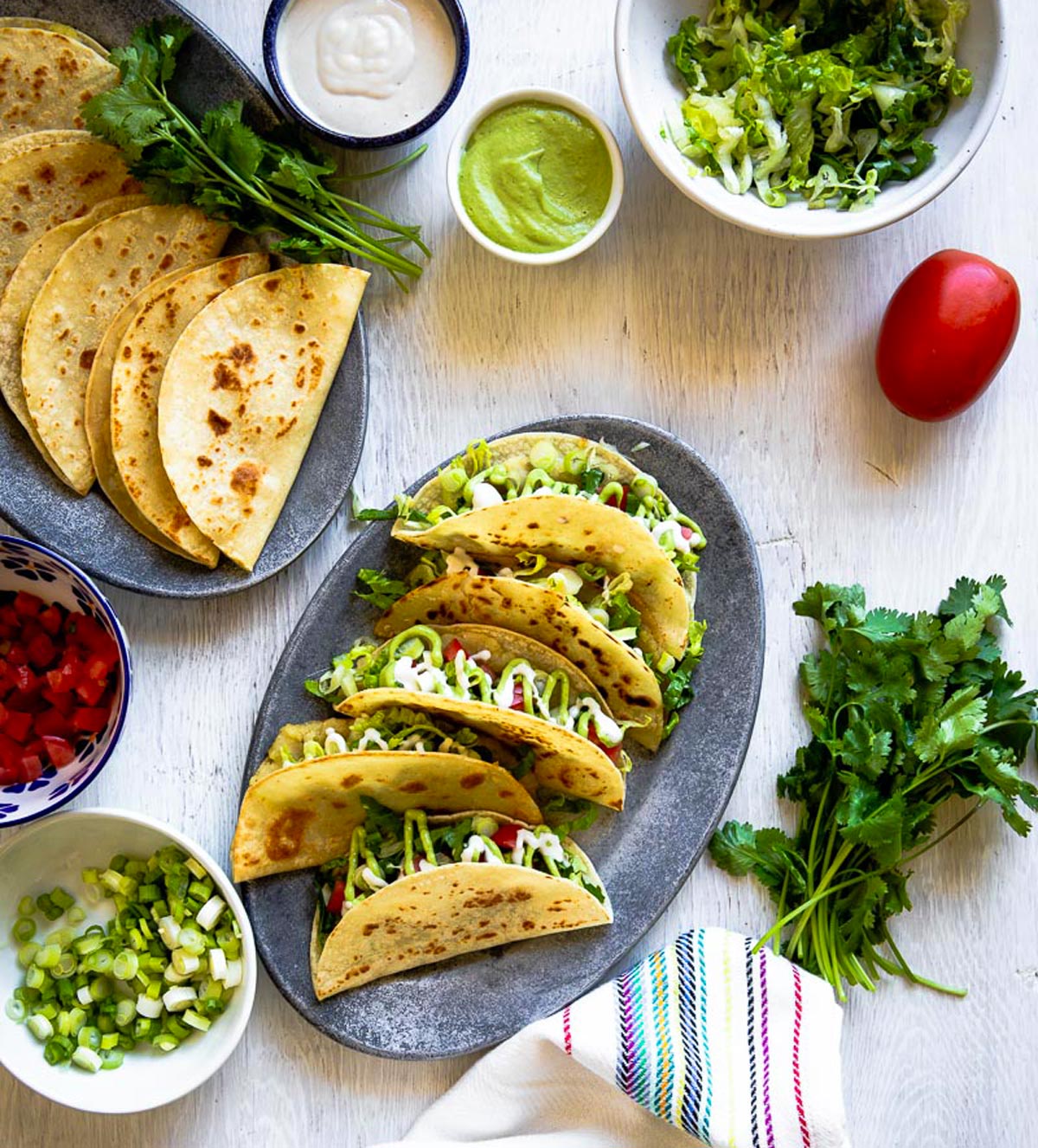 Gray oval plate of tacos de papa topped with avocado crema and cashew cream, showcasing a delicious Mexican tacos recipe.
