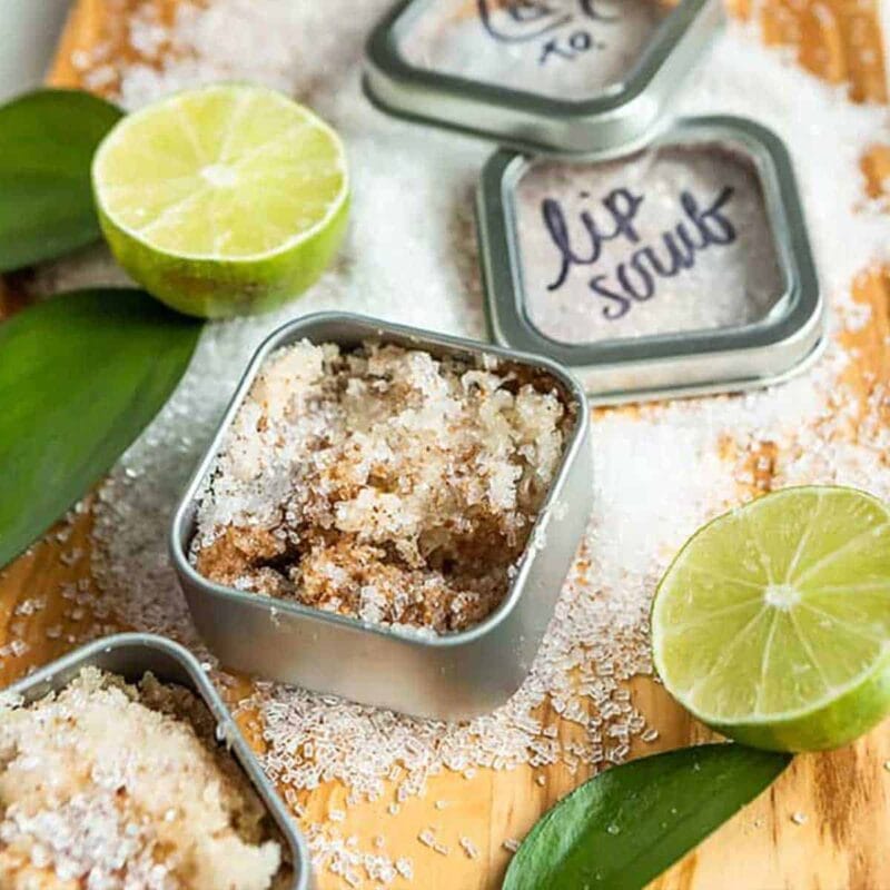 DIY lip scrub in a tin surrounded by limes and sugar.
