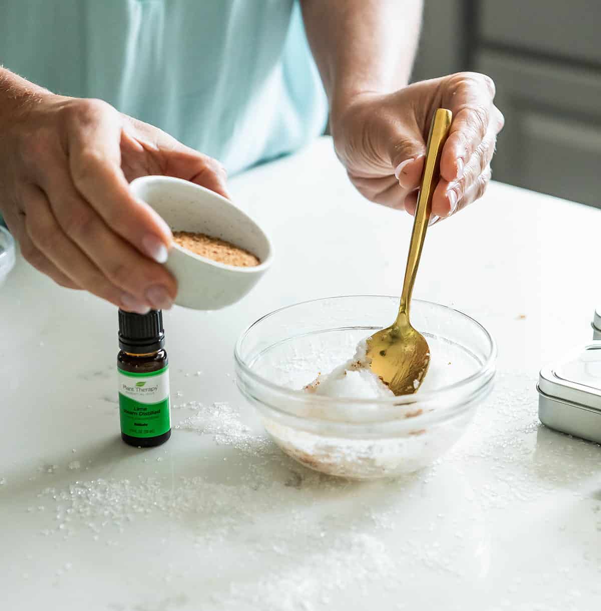 a glass bowl of coconut oil on a counter along with coconut sugar and essential oil.