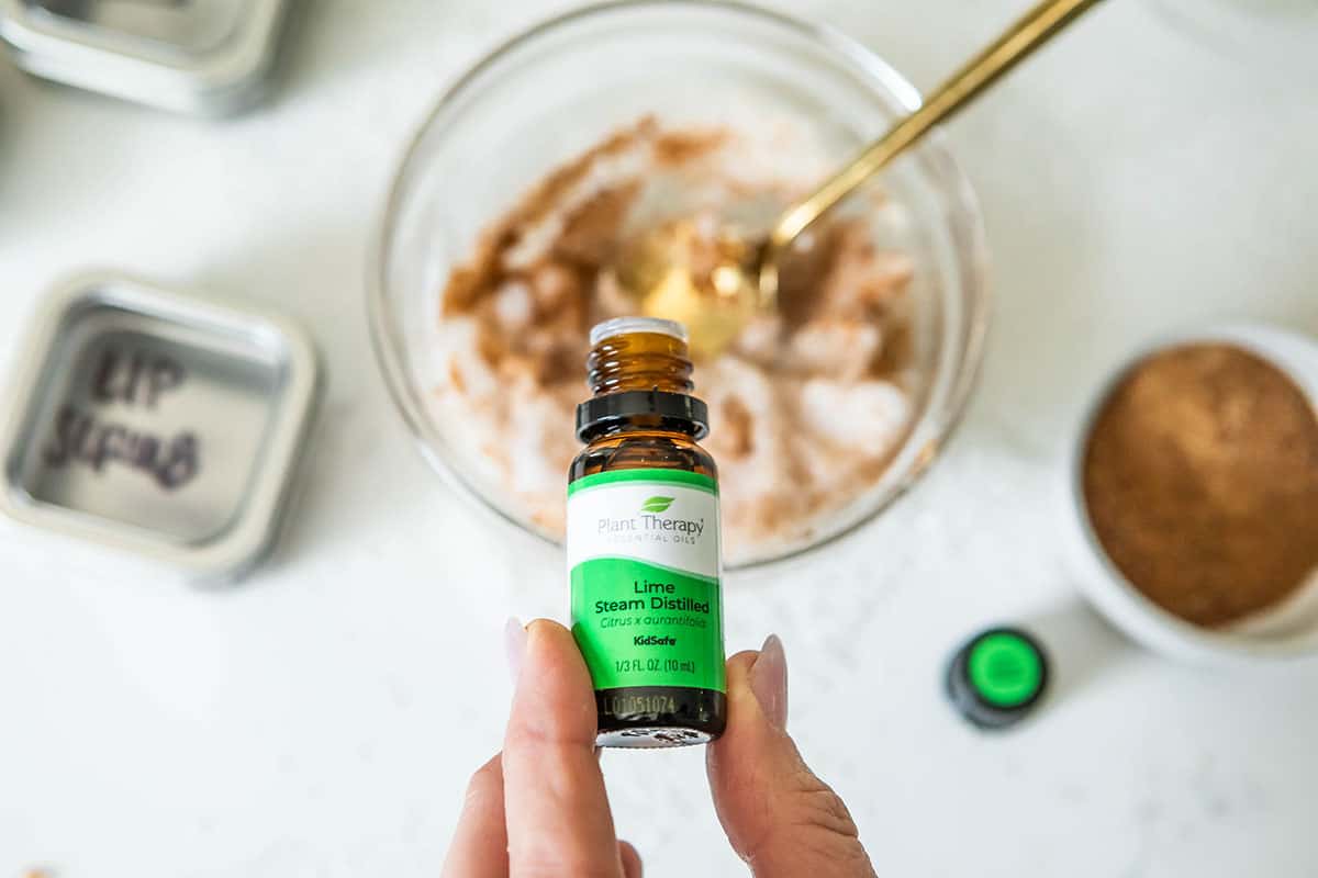 a bottle of steam distilled lime essential oil, pouring into a blurred out bowl of lip scrub mixture.