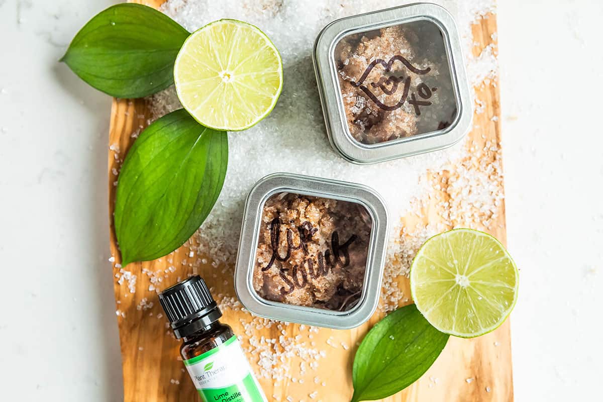 homemade lip scrub in tins next to a sliced lime and a pile of sugar.