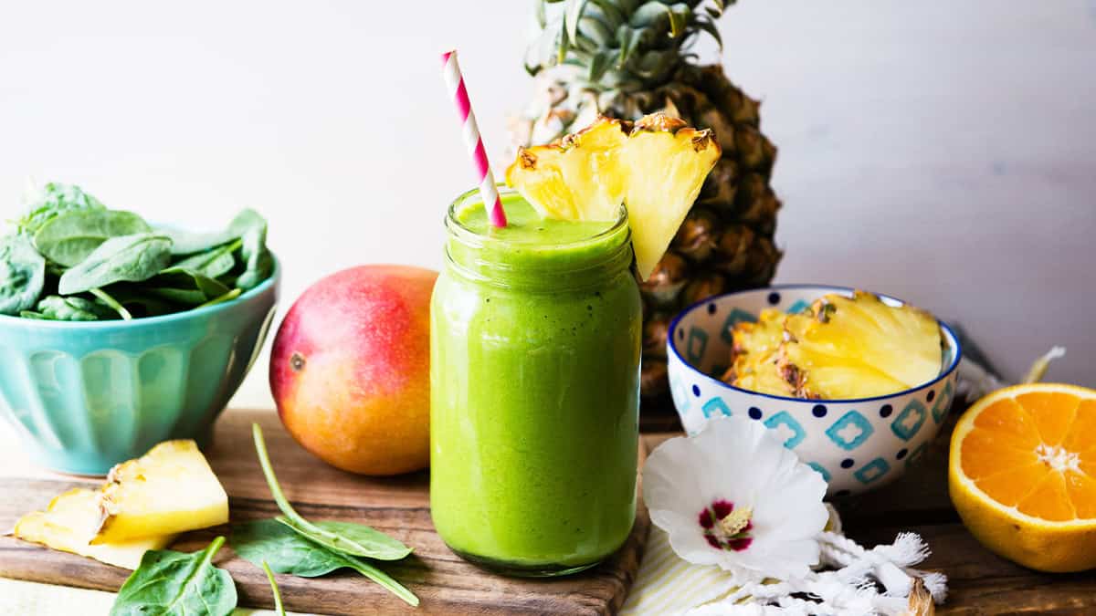 Green detox smoothie with pineapple, mango, and orange on a wooden table