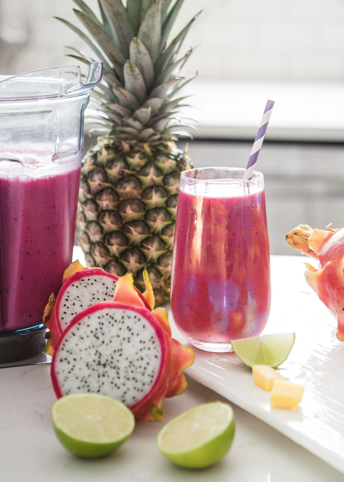 Pink dragon fruit smoothie in a glass, with a blender nearby, showcasing the ingredients used to make it.