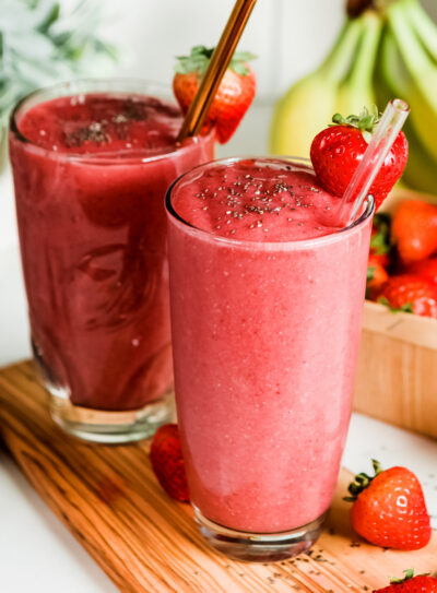 Two vibrant red strawberry banana fruit smoothies in tall glasses, garnished with a strawberry