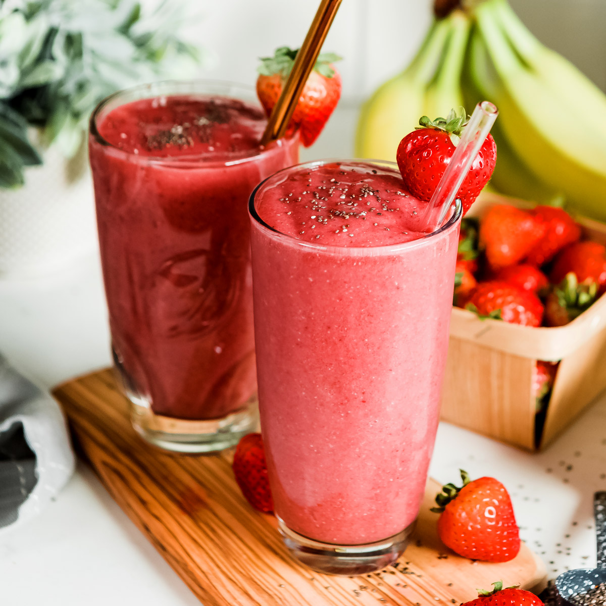 Two vibrant red strawberry banana fruit smoothies in tall glasses, garnished with a strawberry