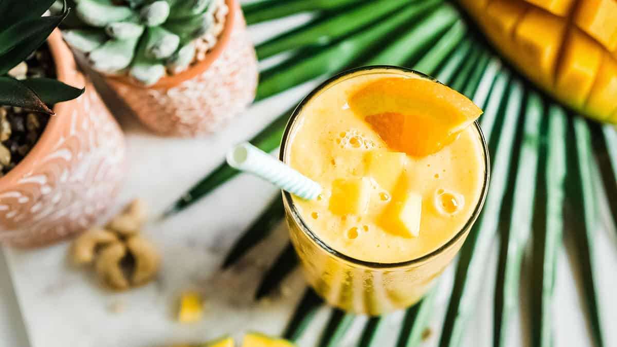 Refreshing mango smoothie with pineapple and ice in a glass with a straw.