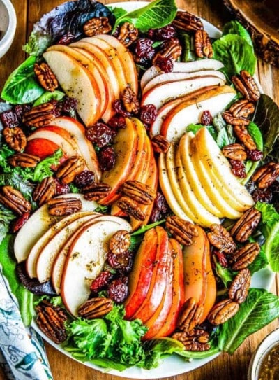 platter of fall salad featuring a bed of mixed greens topped with sliced apples, pears, candied pecans, dried cherries and a vinaigrette.