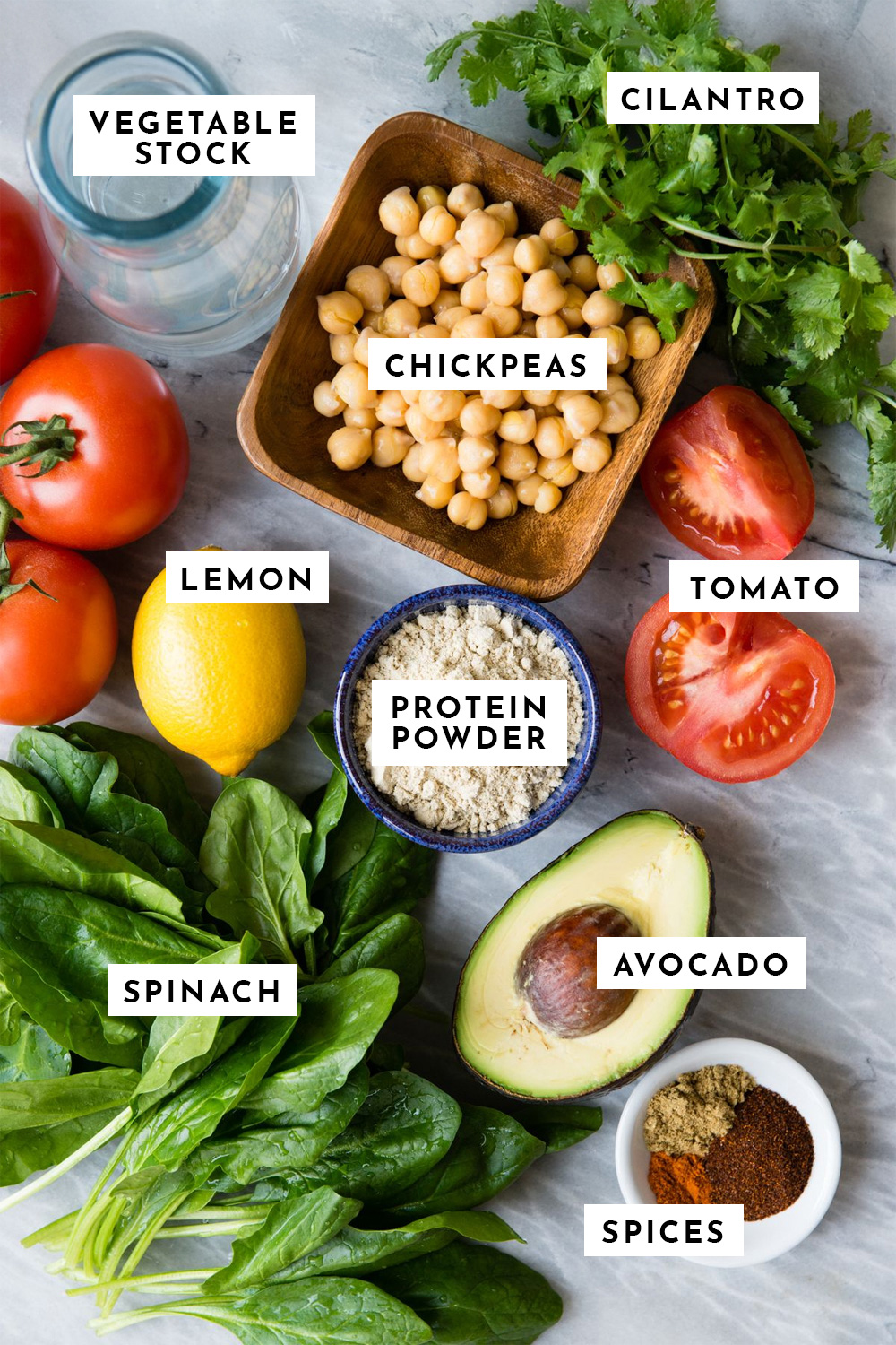 ingredients for a savory smoothie including cilantro, chickpeas, tomato, homemade protein powder, avocado, spices, spinach, lemon juice and vegetable stock.