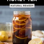 Ginger lemon honey tea for cough home remedy in a glass jar surrounded by sliced ingredients.