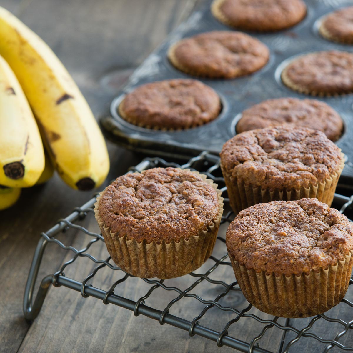 several gluten-free banana muffins on a cooling rack and in a muffin pan.