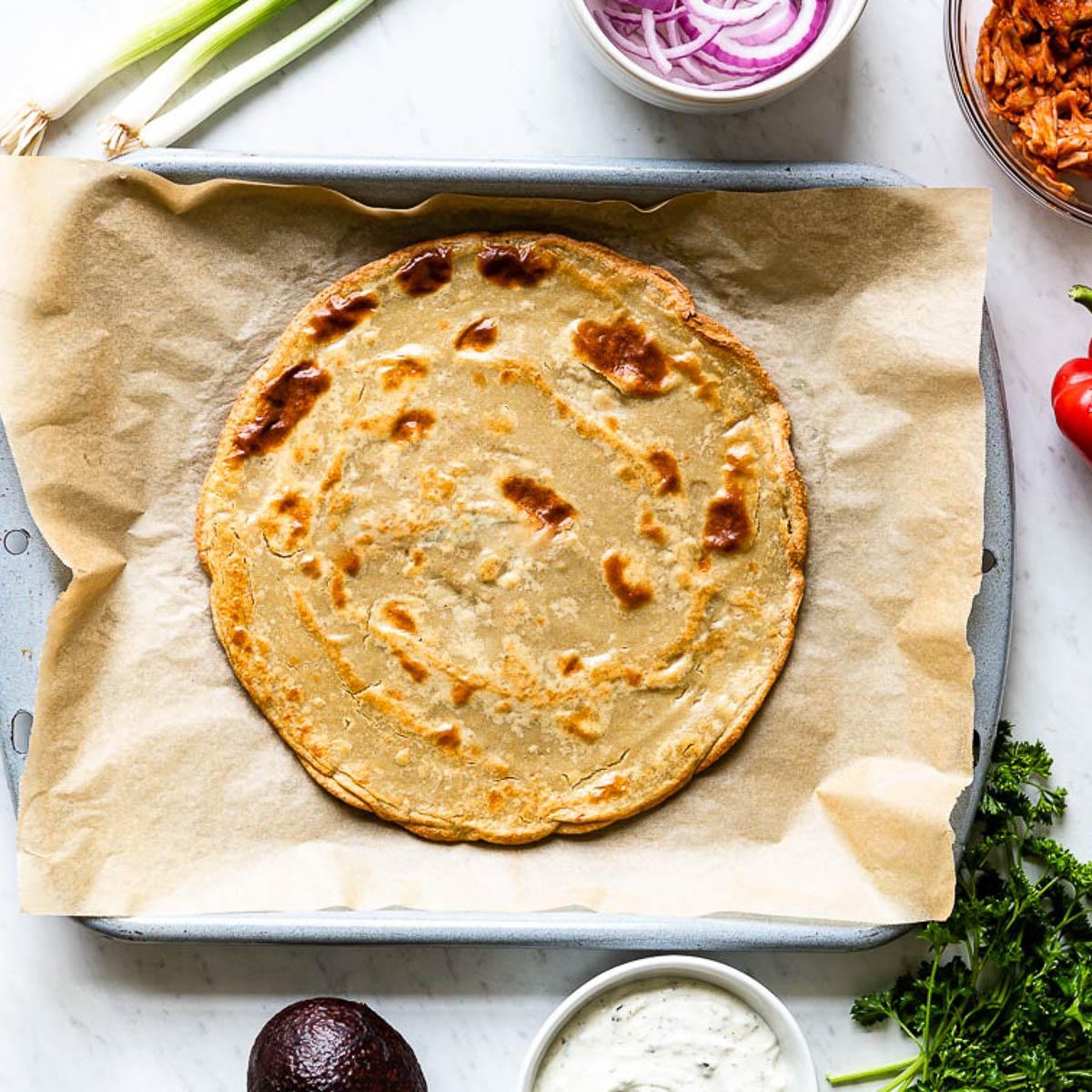 gluten-free pizza crust on a parchment lined baking sheet.