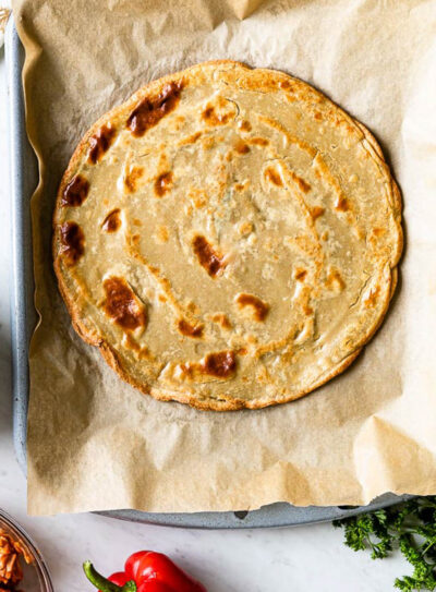 gluten-free pizza crust on a parchment lined baking sheet.