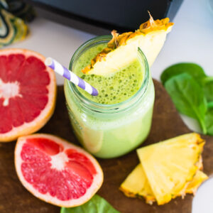 A green energy smoothie with a pineapple wedge surrounded by fresh ingredients.