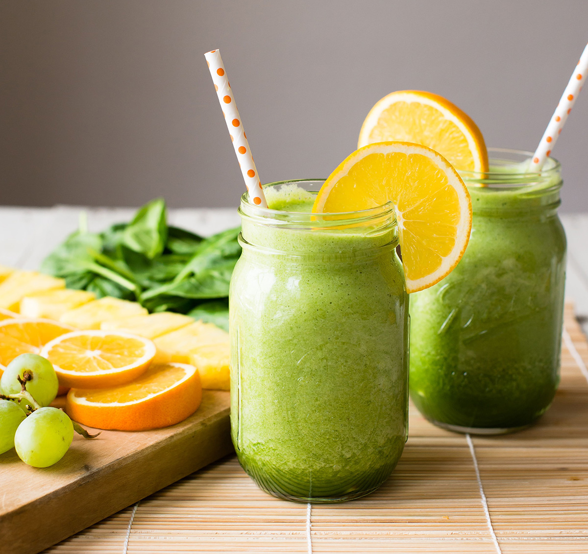 Two glasses of green grape smoothie garnished with orange slice.