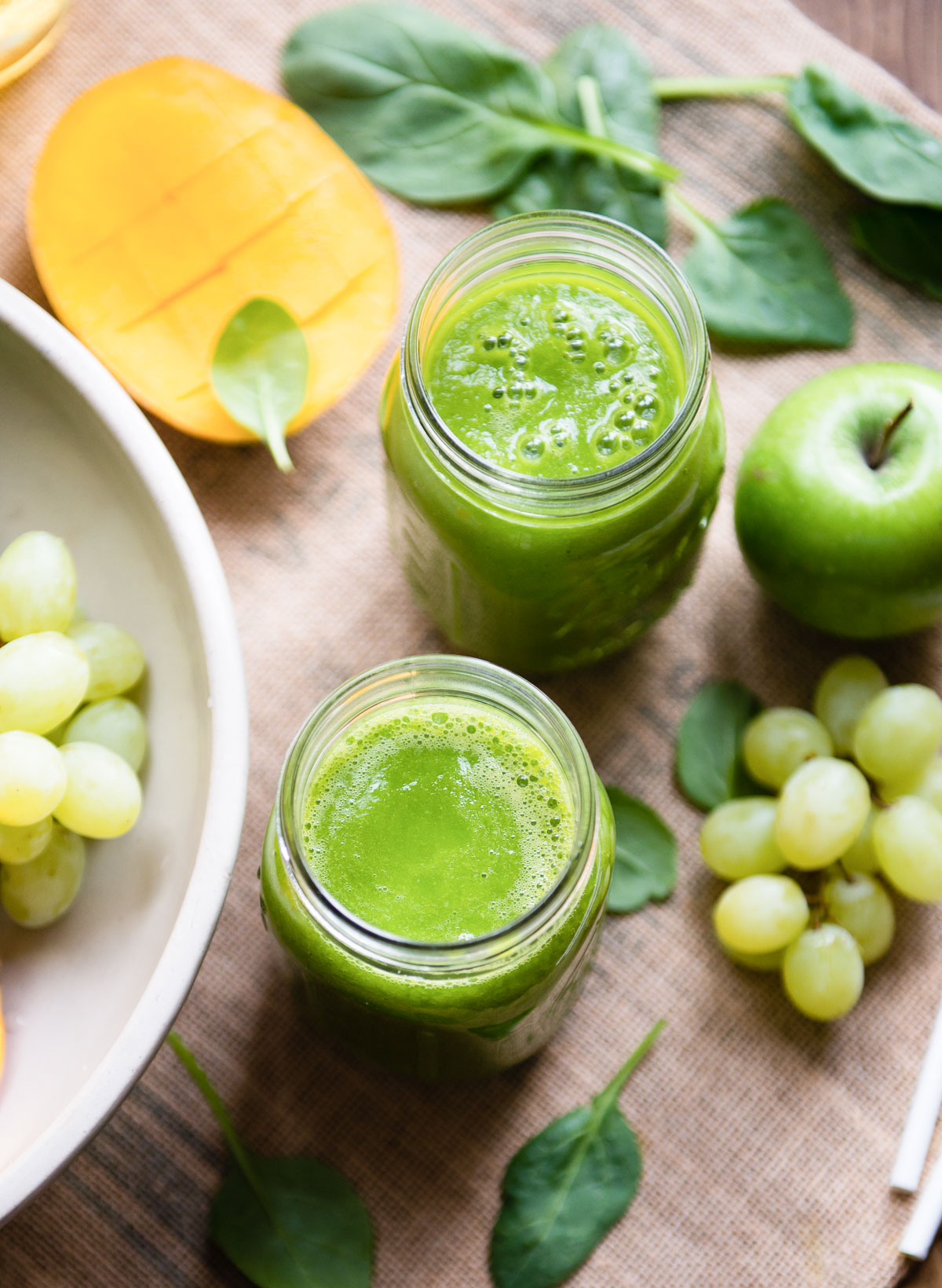 Two Mason jars filled with green tea smoothie surrounded by fresh ingredients. 