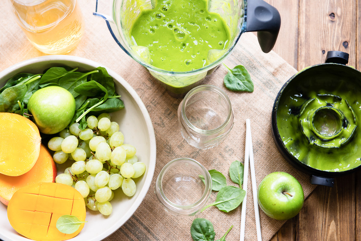 Green tea smoothie in a blender,  two empty glasses, and fresh ingredients