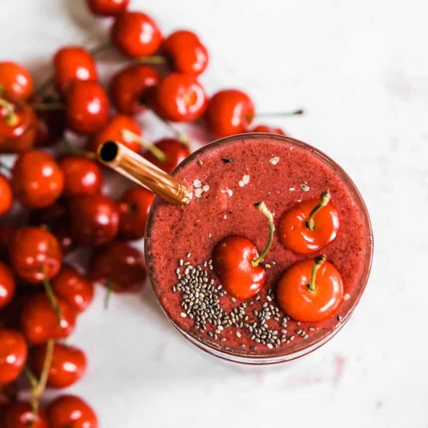 A glass of power cherry smoothie with a straw, topped with fresh cherries and chia seeds.