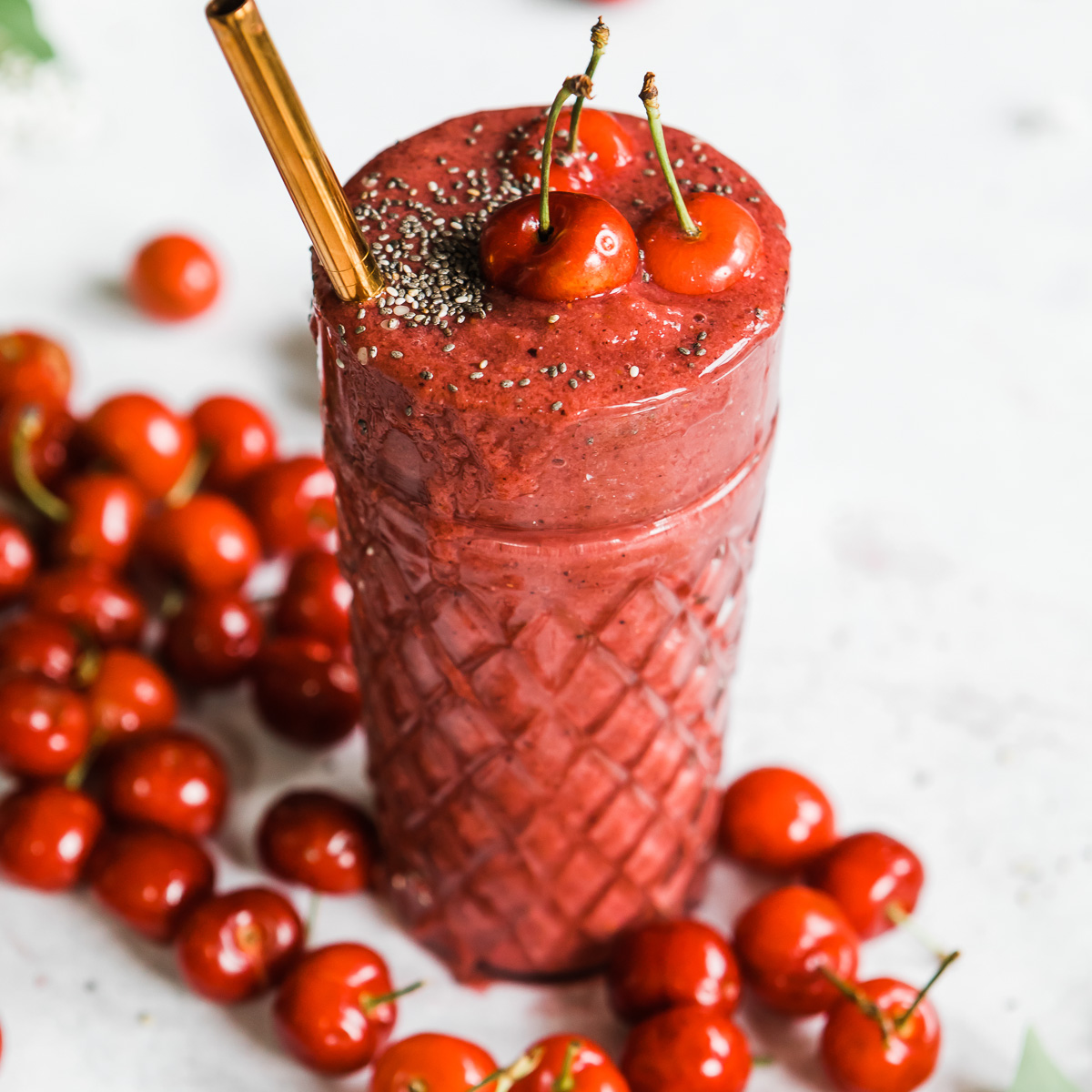 Bright red cherry smoothie in a tall glass.