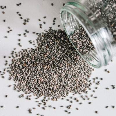 A glass jar laying on its side with spilled chia seeds, highlighting the seeds.