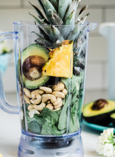 Blender filled with unmixed avocado, pineapple, nuts, and leafy greens.