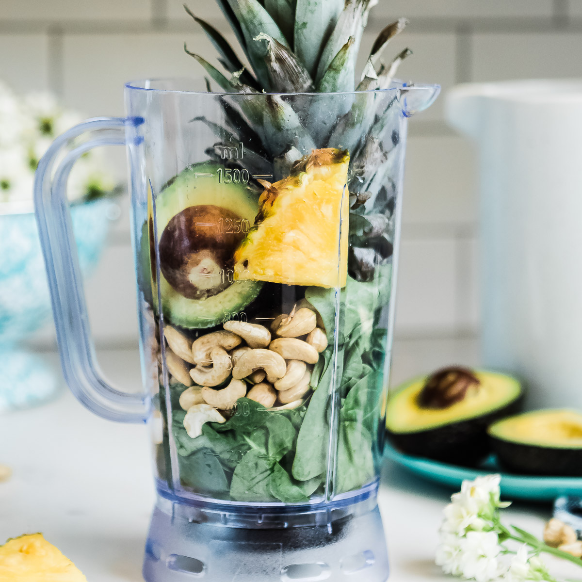 Blender filled with unmixed avocado, pineapple, nuts, and leafy greens.