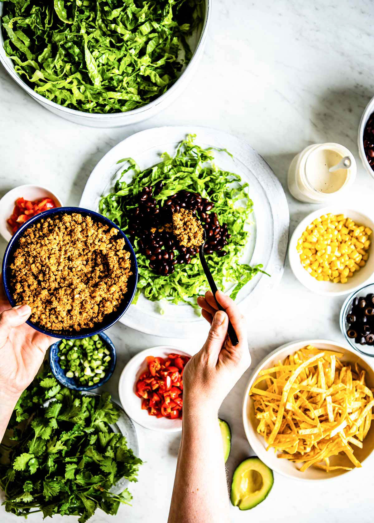 Hands assembling a healthy taco salad with fresh ingredients.