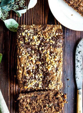 Loaf of healthy zucchini bread with end sliced off next to a knife and a whole zucchini.