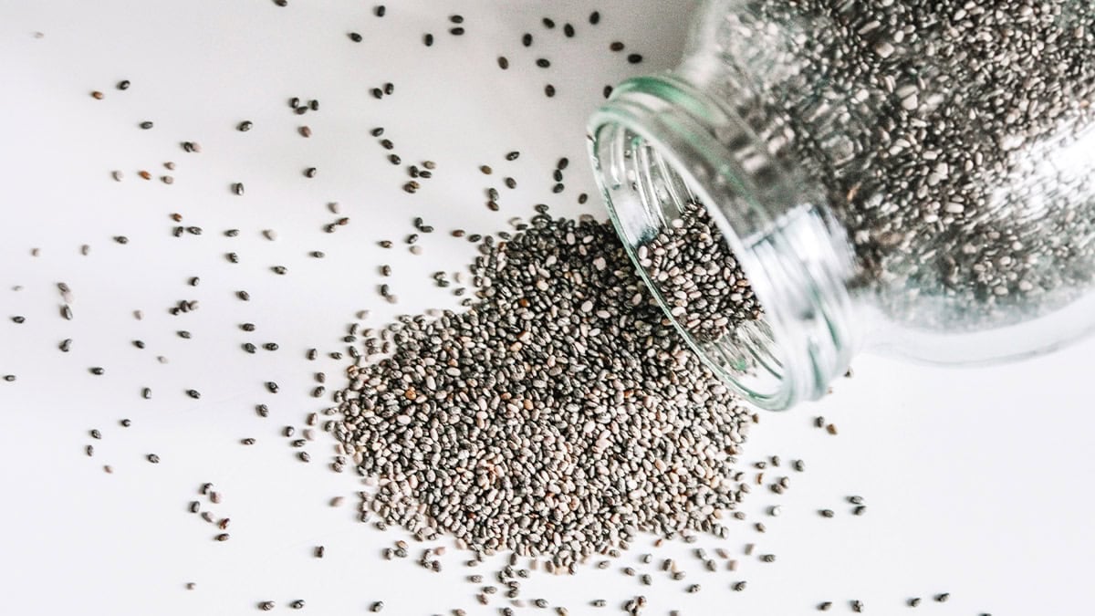 Chia seeds spilling from a glass jar onto a white surface