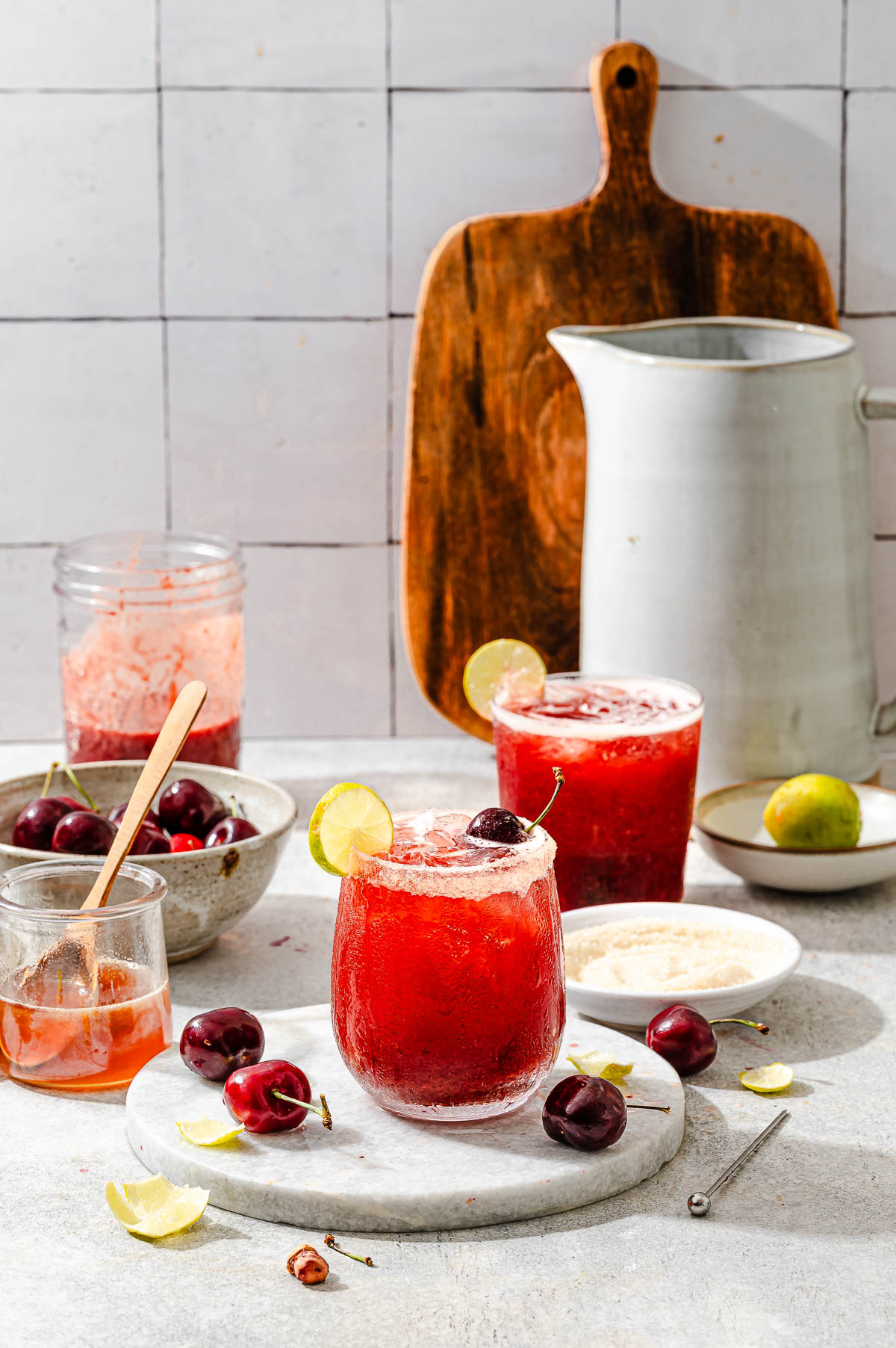 A tabletop view of two glasses of refreshing cherry limeade, complemented by the fresh ingredients used to make it.