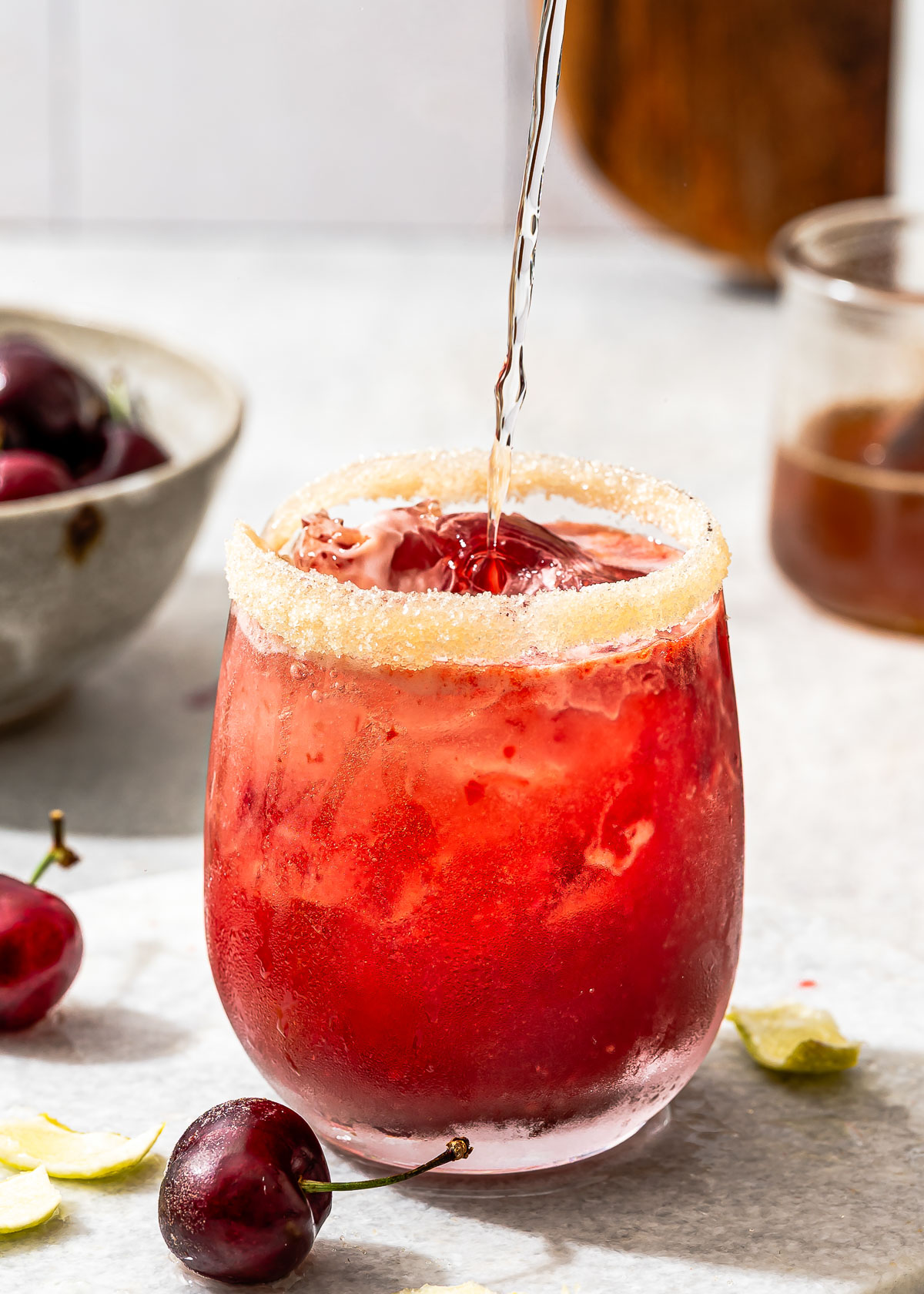 A close-up shot of sparkling water being added to a glass of cherry limeade.