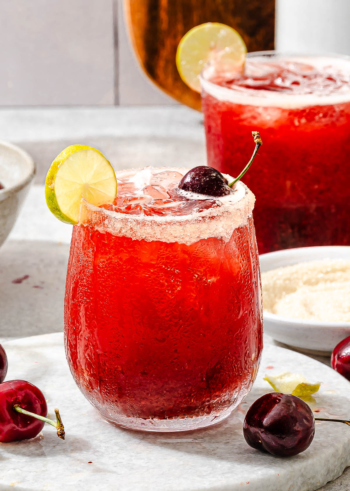 Cherry limeade recipe with a lime wedge and a sparkling sugar rim.