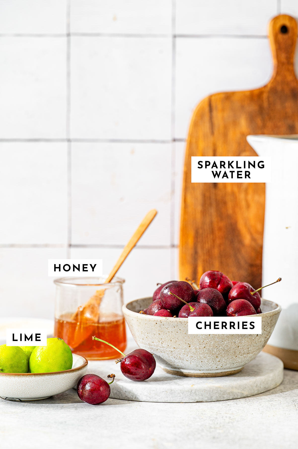 A beautiful arrangement of fresh cherries, sliced limes, honey, and sparkling water, to make cherry limeade recipe.