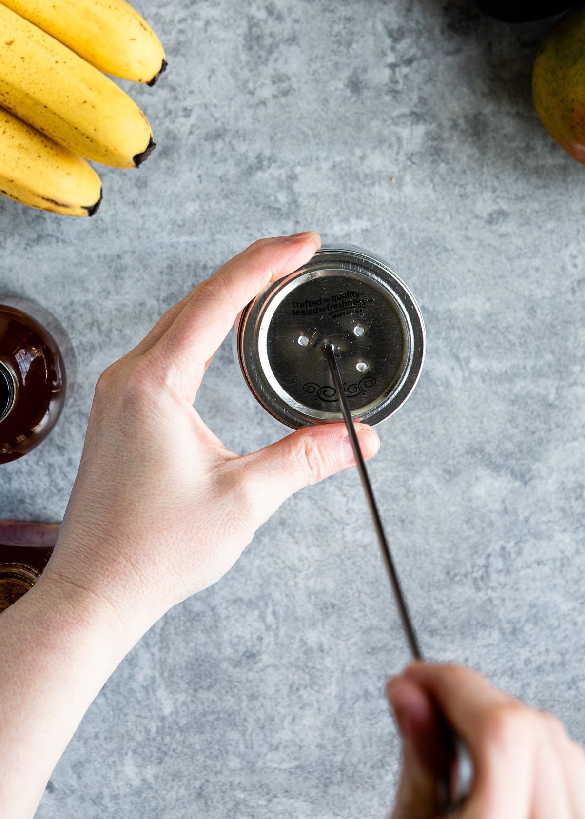 A person poking holes in a mason jar lid.