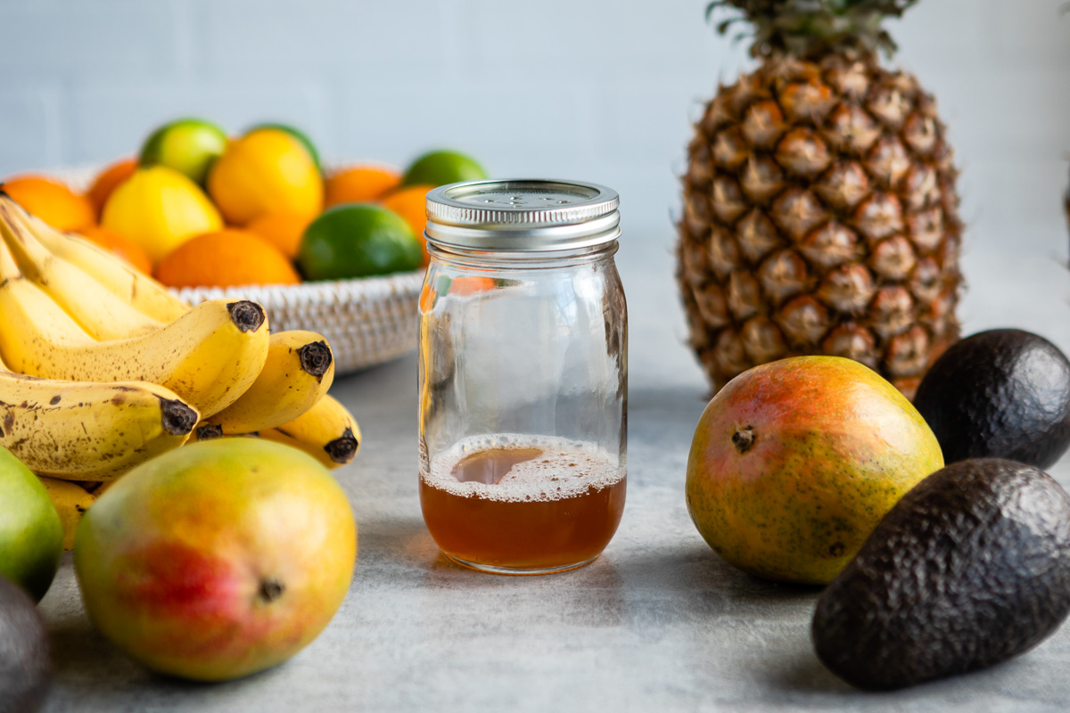 Homemade fruit fly trap jar surrounded by fresh fruits.