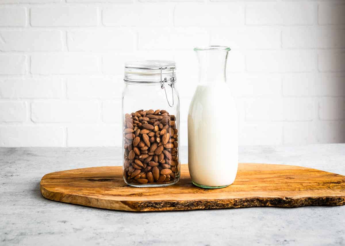 homemade nut milk next to a glass jar of raw almonds on a wooden board.